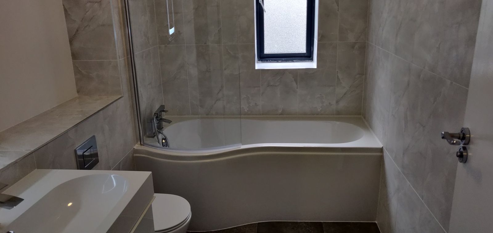 Finished bathroom refit with marble-effect tiles, P-shaped bath and glass screen