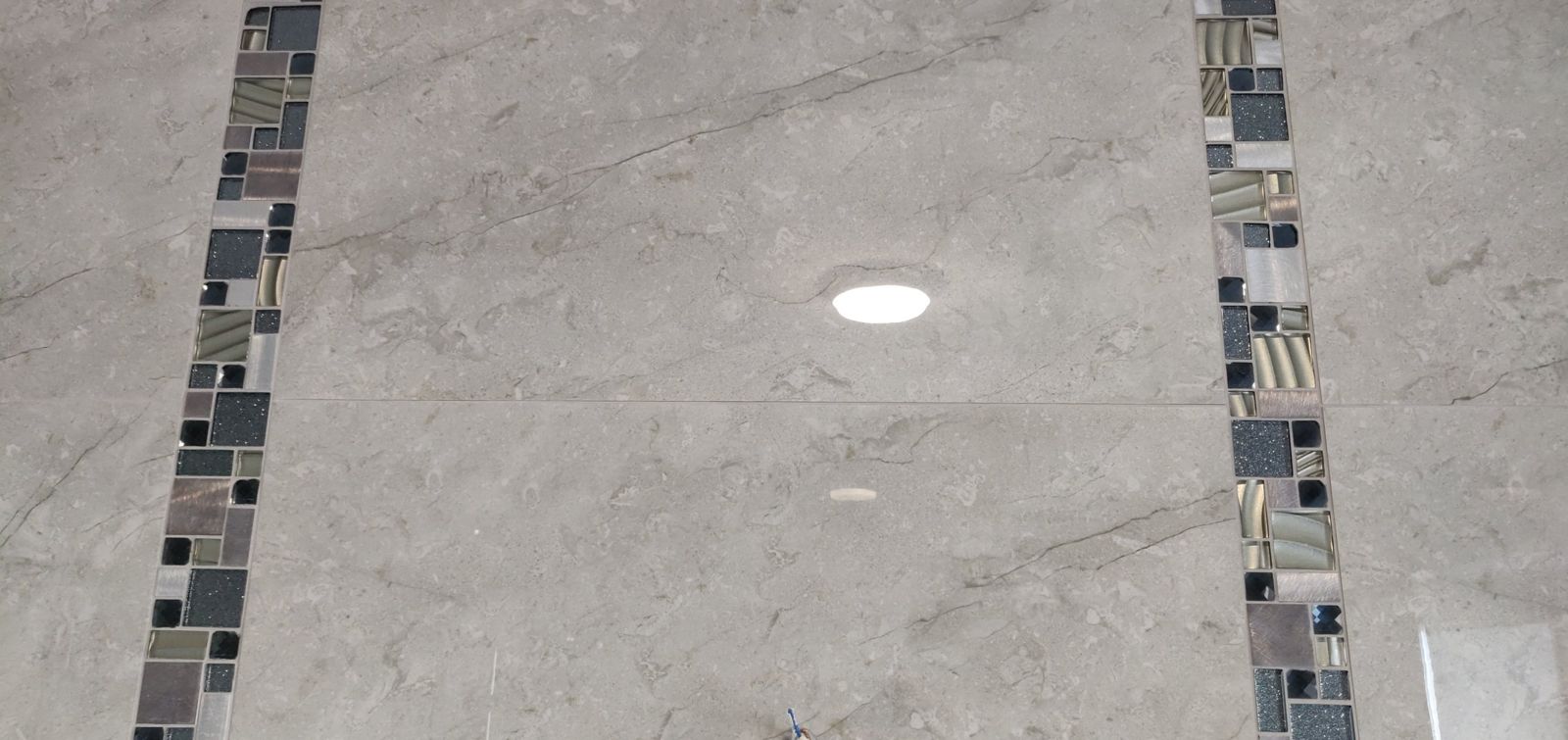 Detail of large marble-effect tiles with glass mosaic strips
