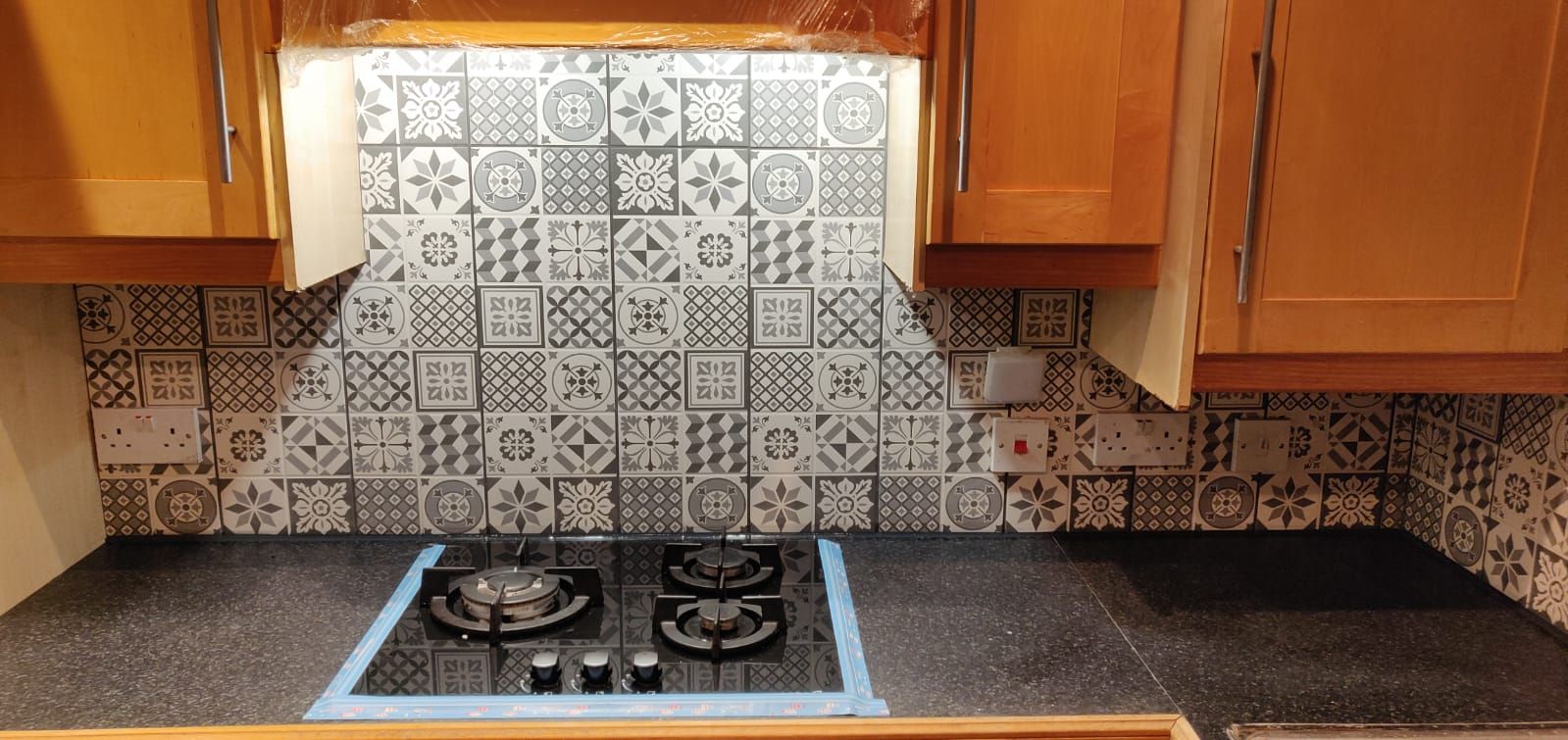 New patterned grey and white kitchen splashback tiles behind a gas hob