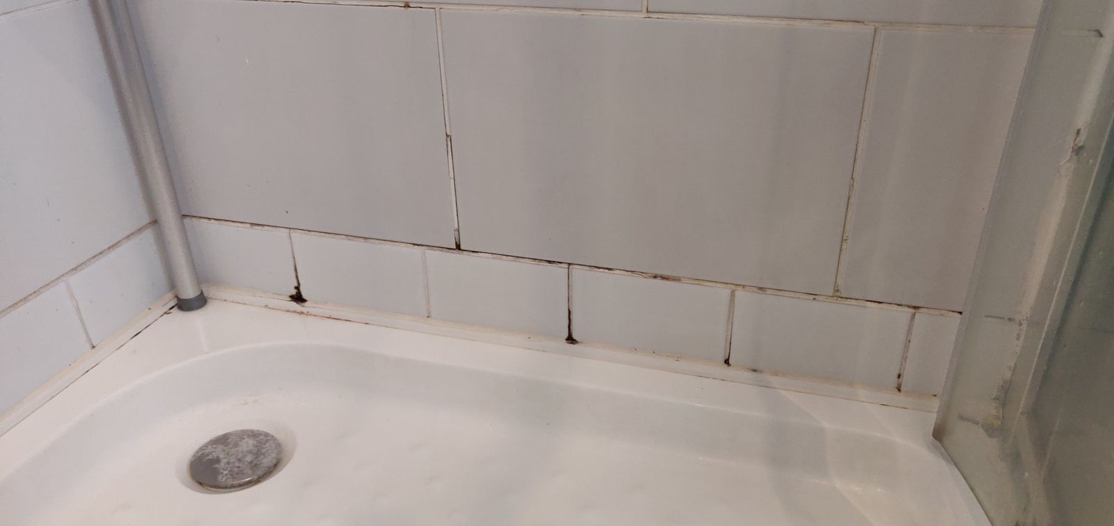 Shower before: cracked tiles and black mouldy grout along the tray